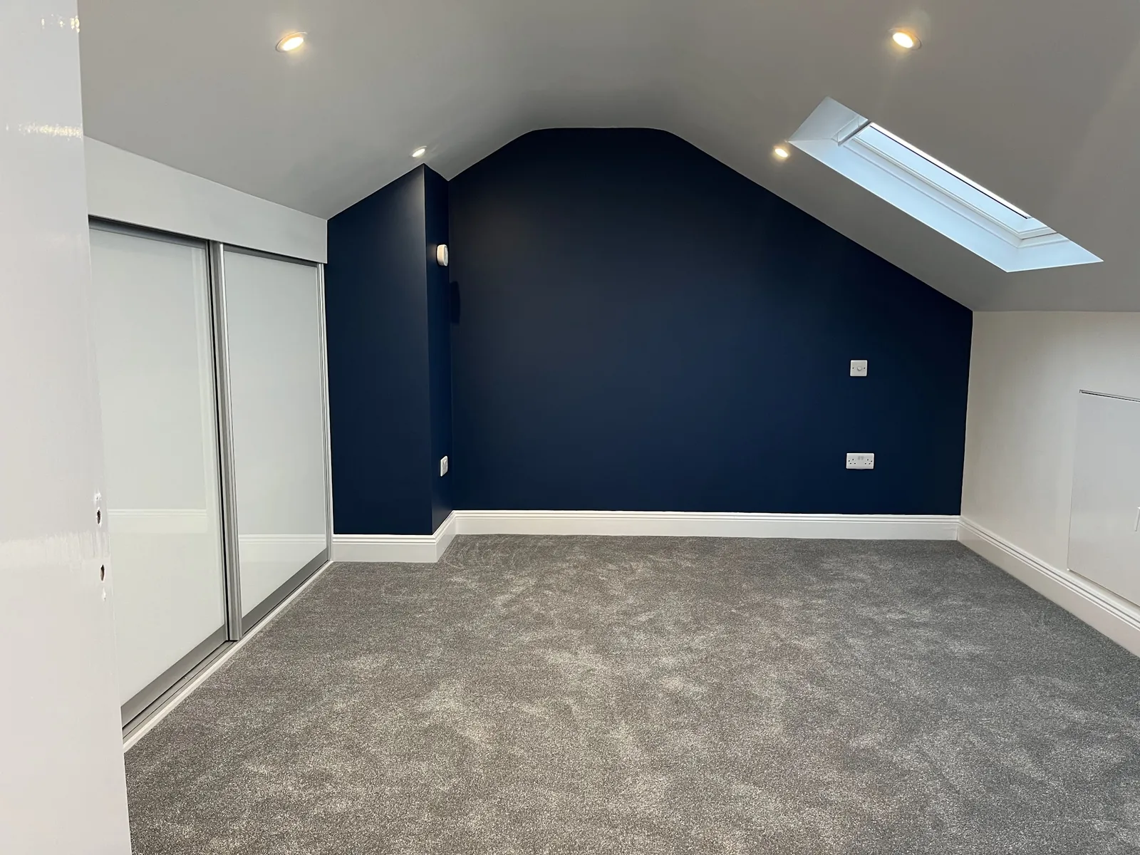 Attic bedroom with navy feature wall, Velux and grey carpet